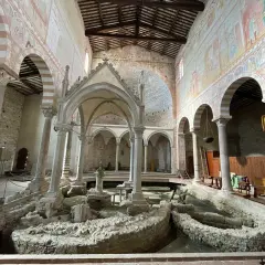 Interno della Basilica di San Piero a Grado, con affreschi medievali e resti archeologici al centro.
