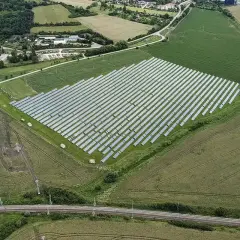 Widok z lotu ptaka na dużą farmę paneli słonecznych otoczoną polami i lasem.