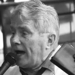 Luis Palau spricht ins Mikrofon, hält eine Bibel und eine Brille.