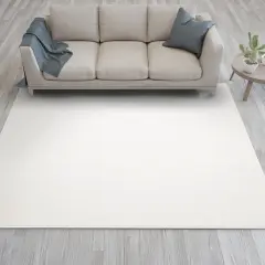 Jasna sofa w kolorze kość słoniowa, z niebieskim kocem i poduszką, stoi na jasnym dywanie. Obok stolik z kaktusem.