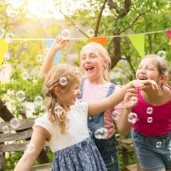 Trzy dziewczynki śmieją się i łapią bańki mydlane w ogrodzie. Wesołe życzenia urodzinowe dla dziecka!