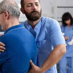 Fizjoterapeuta pomaga pacjentowi z bólem pleców i mięśni. W tle szkielet i pielęgniarka.