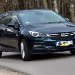 Ciemnozielony Opel Astra K 1.4 Turbo jedzie po drodze wśród drzew.