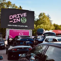 Bilar samlade vid en solvalla drive in bio. Stor skärm visar "DRIVE-IN FILM Stockholm Festival".