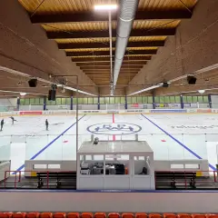 Eishalle Wiehl mit Eisfläche, Banden und Tribüne. Einige Eisläufer sind auf dem Eis zu sehen.