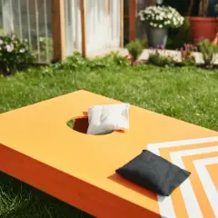 Orange Cornhole-Brett mit weißen Streifen, bereit für das Spiel. Perfekt für das **cornhole selber bauen** im Garten.