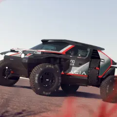Un Dacia Sandrider nero e rosso sfreccia su un terreno sabbioso, pronto per l'avventura nel deserto.