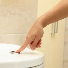 Dłoń naciska przycisk spłuczki. Szukasz domowych sposobów na zbyt częste oddawanie moczu?