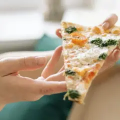 Kawałek pizzy z pomidorkami i szpinakiem, trzymany w dłoniach. Tak jeść pizzę we Włoszech – delektując się każdym kęsem.