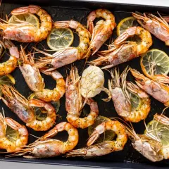 Gamberoni al forno dorati e succulenti, conditi con erbe aromatiche e fette di limone, pronti per essere gustati.
