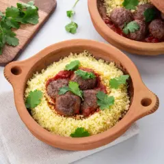 Délicieuse recette de boulette de boeuf haché avec sauce, servie sur un lit de couscous et garnie de coriandre fraîche.