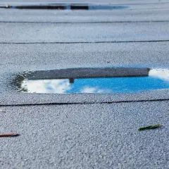 Pfützen auf Bitumenschindeln: Was tun bei undichten Stellen? Wasser sammelt sich auf dem Dach, ein Zeichen für mögliche Schäden.
