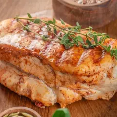 Soczysty filet z indyka duszony, z gałązką tymianku i pomidorkami koktajlowymi na desce.