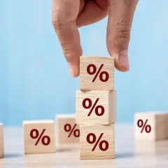 Main d'une personne empilant des cubes en bois marqués du symbole "%", symbolisant le calcul du taux de remplacement retraite.