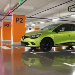 Une voiture verte est garée en bataille dans un parking souterrain, avec des poteaux orange marqués "P2".
