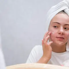 Dziewczyna z ręcznikiem na głowie nakłada maść z witaminą A na twarz, licząc na jej efekty w walce z niedoskonałościami.