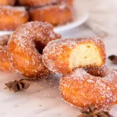 Rosquillas de carnaval espolvoreadas con azúcar, una con un mordisco, junto a anís estrellado.