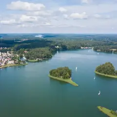 Malownicze jeziora w Polsce, z zielonymi wyspami i żaglówkami, otoczone lasami i domkami letniskowymi.