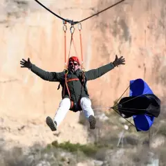 Hombre disfrutando de una tirolina de cuenca, con los brazos extendidos y una gran sonrisa, mientras desciende por un acantilado.