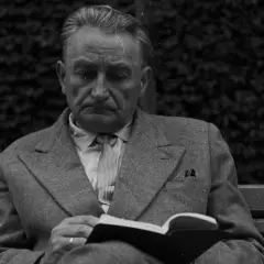 Zamyślony mężczyzna w garniturze czyta książkę na ławce. Może w tej chwili myśli, że życie mnie mnie fraszka, szukając ukojenia w literaturze.