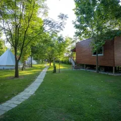 Glamping w Albanii, blisko morza jońskiego. Białe namioty i drewniany domek na wzgórzu, otoczone zielenią.
