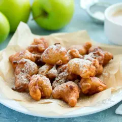 Montón de buñuelos de manzana dorados y espolvoreados con azúcar glas, listos para disfrutar.