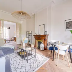 Salon lumineux avec canapé gris, tapis graphique, cheminée ancienne et table à manger. Une belle idée home staging pour un espace convivial.