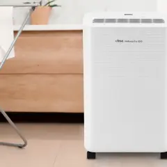 Un deshumidificador Ufesa Wellness Dry 2000, blanco y con ruedas, junto a un tendedero con ropa.