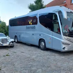 Biała limuzyna i szary autokar stoją obok siebie na brukowanym dziedzińcu.