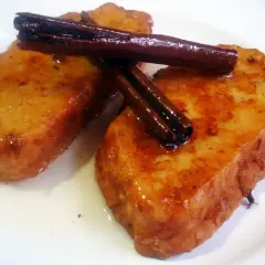 Dos deliciosas torrijas de vino, doradas y bañadas en almíbar, coronadas con canela en rama.