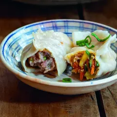 Dwa pierogi gyoza z mięsem i warzywami w miseczce na drewnianym stole.