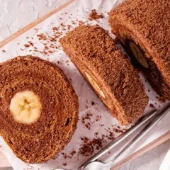 Czekoladowe ciasto gąbka z bananem w środku, pokrojone na plastry, posypane wiórkami.