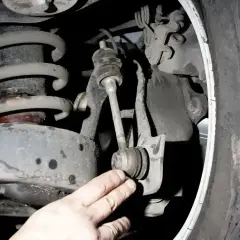 Dłoń mechanika wskazuje na zużyte tuleje stabilizatora w zawieszeniu samochodu.