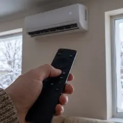 Mano con mando a distancia ajustando el icono de calor en aire acondicionado. Afuera, ventanas con nieve.