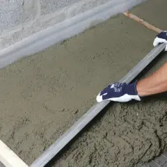 Ręce w rękawiczkach wyrównują świeży styrobeton lambda za pomocą łaty.