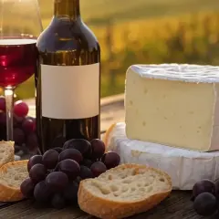Un verre de vin rouge, une bouteille, du pain, des raisins et du fromage. La question est : que boire avec du fromage pour un moment parfait ?
