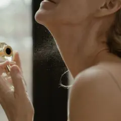 Kobieta aplikuje perfumy na szyję, tworząc mgiełkę zapachu. To idealne miejsce, gdzie psikac perfumami, by subtelnie podkreślić swoją obecność.
