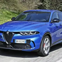 Niebieski Alfa Romeo Tonale pędzi po drodze. Wśród wielu marek samochodów alfabetycznie, ten włoski SUV wyróżnia się dynamicznym designem.
