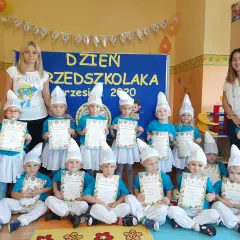 Dzieci w strojach smerfów z dyplomami, z nauczycielkami w tle.