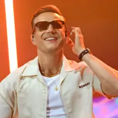 Artysta Mrozu w okularach przeciwsłonecznych, na scenie, z podświetleniem.