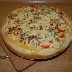 Pizza z kukurydzą, papryką i grzybami, polana obficie białym sosem do pizzy, na drewnianym blacie.