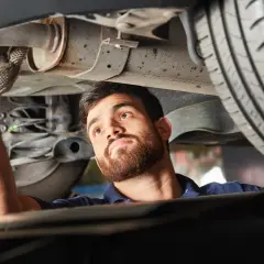 Mechanik w rękawiczce sprawdza podwozie samochodu, wykonując naprawę układu wydechowego.