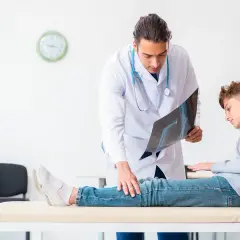 Arzt erklärt Röntgenbild einem Jungen, der auf einer Liege sitzt. Möglicherweise geht es um Orthese Druckstellen.
