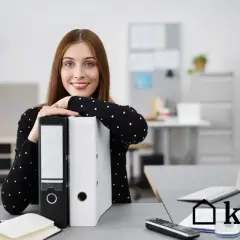 Uśmiechnięta kobieta w biurze opiera się o segregator.