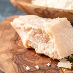 Kawałek twardego sera, przypominającego Grana Padano i parmezan, leży na drewnianej desce.