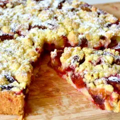 Saftiger Zwetschgenkuchen mit Streuseln, nach Omas Rezept. Ein Stück ist herausgeschnitten und zeigt die fruchtige Füllung.