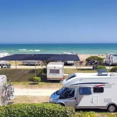 Autocaravanas y caravanas en un camping junto al mar, ideal para camping en Barcelona. El mar azul y la playa invitan a disfrutar del sol.