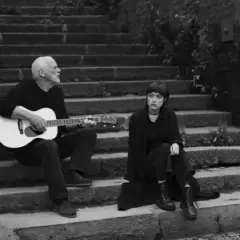 David Gilmour gra na gitarze, a obok niego siedzi jego córka.