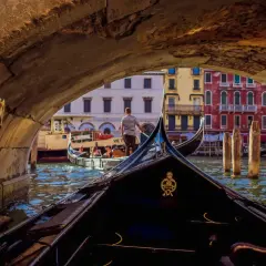 Widok z gondoli pod mostem w Wenecji. W oddali kolorowe kamienice i inna gondola.