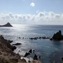 Costa rocosa con formaciones volcánicas emergiendo del mar azul. El arrecife San José se alza majestuoso, reflejando el sol.